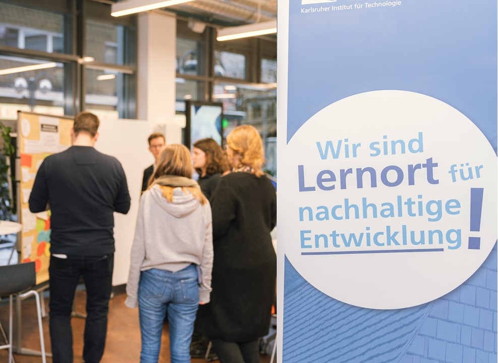 KIT Banner des KIT mit dem Text „Wir sind Lernort für nachhaltige Entwicklung“ vor einer Personengruppe.
