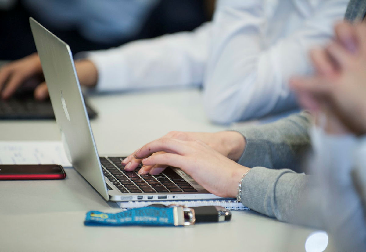 Person tippt auf einem Laptop in einem Bürosetting.